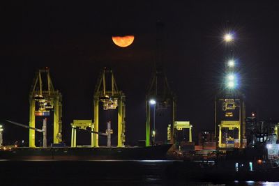 Cranes at harbor against sky during night