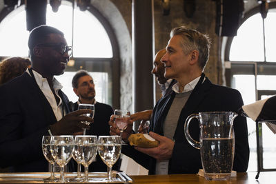 Businessmen holding glasses while discussing with each other during seminar