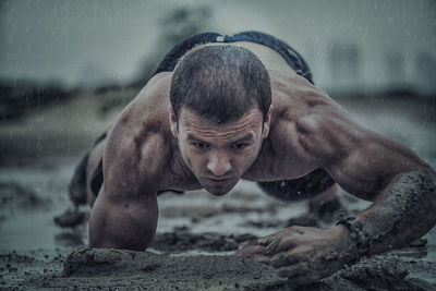 Close-up of athletic man exercising in mud during rainy season