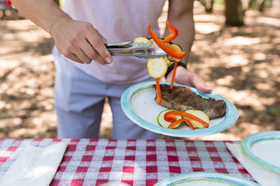 Cropped image of man holding vegetables in serving tongs at table