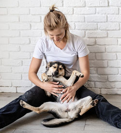 Young woman with dog sitting against wall