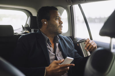 Male entrepreneur with mobile phone and insulated drink container sitting in car