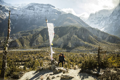 Male hiker standing near white flag in mountainous valley in himalayas on sunny day in nepal