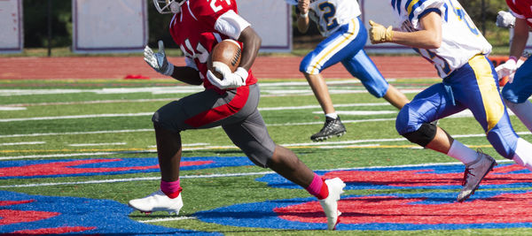 A high school football player is running with the ball being chased by the defensive players.