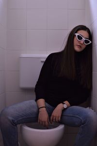 Portrait of young woman in sunglasses sitting on toilet bowl