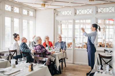 Owner clicking photograph of senior friends sitting in restaurant