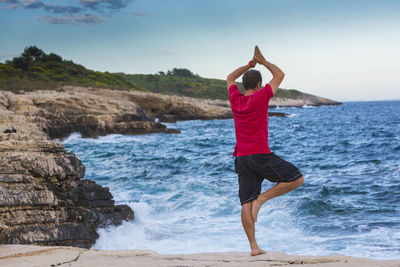 Rear view full length of man practicing tree pose against sea