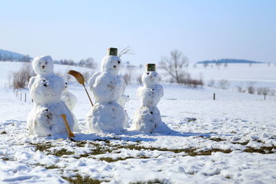 Close-up of snowmen on field against sky