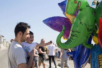 Father and son by inflatable balloon against blue sky