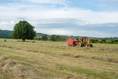Tractor with bailing trailer working on the field gathering grass for gay bales