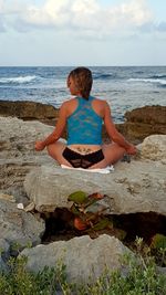 Rear view of woman exercising on rocky beach