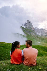 Rear view of couple sitting on mountain against sky