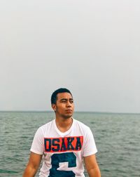 Young man standing in sea against sky