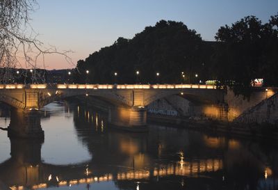 Illuminated bridge over river in city at night