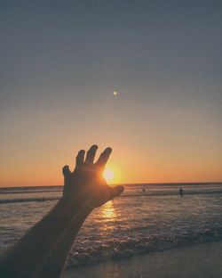 Man hand on beach against sky during sunset