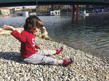 Cute boy sitting at lakeshore in city