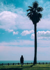 Silhouette woman by palm tree against sky