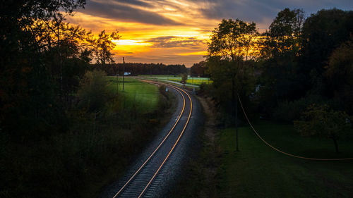 Railroad tracks amidst trees against sky during sunset