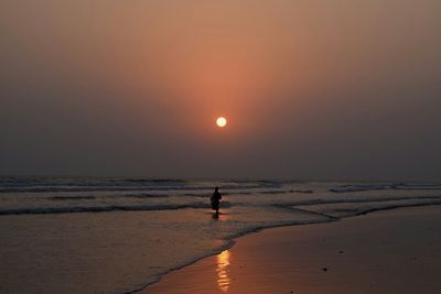 Silhouette person standing on beach against sky during sunset