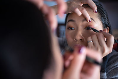 Asian woman applying eyeliner in front of mirror