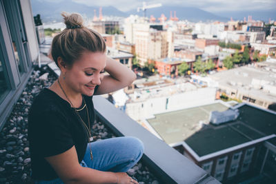 Young woman looking away while sitting against city