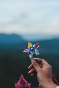 Cropped hand holding pinwheel toy against sky