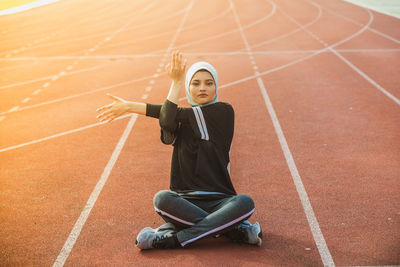 Portrait of female athlete stretching while sitting on track