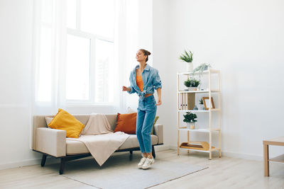 Full length of young woman sitting on bed at home