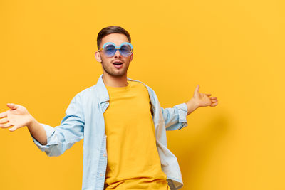 Young woman wearing sunglasses while standing against yellow background