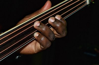 Cropped hand of man playing guitar against black background