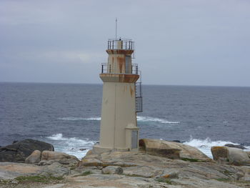 Lighthouse on rock by sea against sky