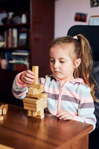Little girl preschooler playing with wooden blocks toy building a tower. concept of building a house