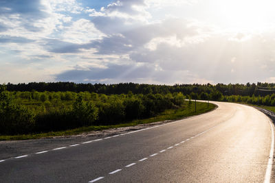 Empty road along trees and landscape against sky