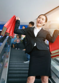 Smiling woman holding shopping bags while standing on escalator