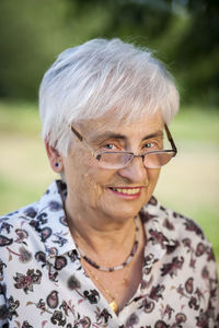 Portrait of old woman with white hair in a park looking over the edge of her glasses.