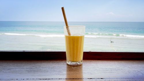 Close-up of drink on table at beach against sky