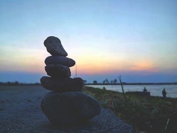 Stack of pebbles on beach against sky during sunset