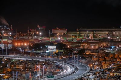 Light trails on street amidst illuminated cityscape against sky at night