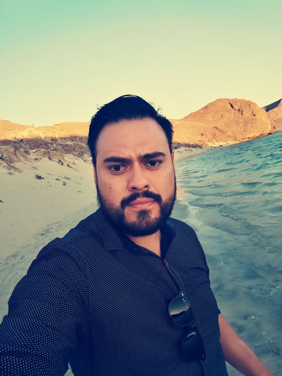 real people, looking at camera, nature, leisure activity, portrait, front view, sand, outdoors, clear sky, sea, scenics, lifestyles, mountain, one person, water, day, beauty in nature, vacations, beard, beach, young adult, sky