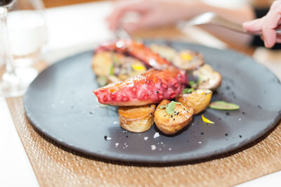 Midsection of person eating tentacles served on table at restaurant