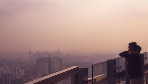 Man standing by railing in city against sky