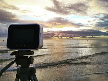 Camera at beach against sky during sunset