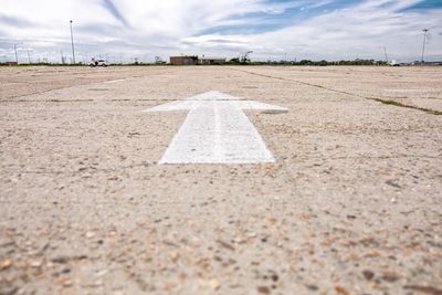 Arrow symbol on pathway against cloudy sky