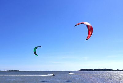 People kiteboarding on sea against blue sky during sunny day