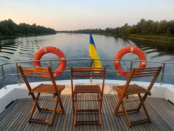 Deck chairs on railing by lake against sky