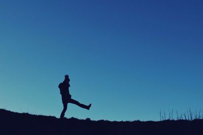 Silhouette woman kicking on field against clear blue sky