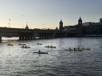 People on river by city against sky