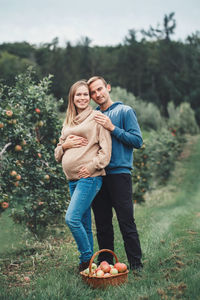 Portrait of smiling pregnant couple standing by apples in basket