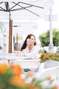 Adult smiling brunette woman forty years using mobile phone in cafe at city street