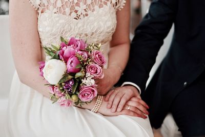 Midsection of bride holding flower bouquet while holding hand of husband